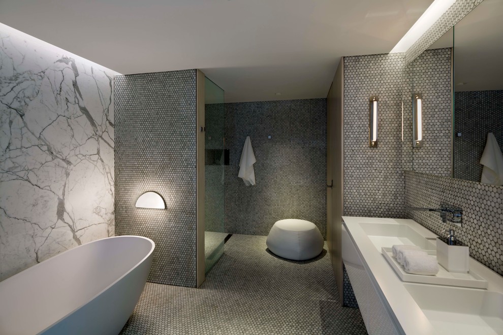 Modern inredning av ett mycket stort en-suite badrum, med släta luckor, vita skåp, ett fristående badkar, en öppen dusch, vit kakel, stenkakel, vita väggar, klinkergolv i småsten, ett integrerad handfat och bänkskiva i akrylsten