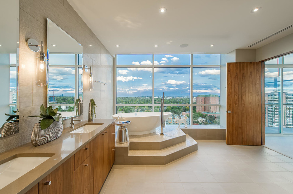 This is an example of a contemporary bathroom in Denver with flat-panel cabinets, medium wood cabinets, a freestanding bath, beige tiles and a submerged sink.