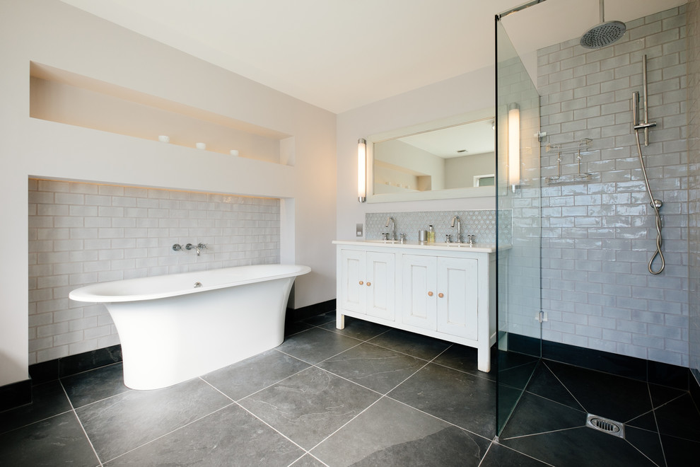 コーンウォールにあるトランジショナルスタイルのおしゃれなマスターバスルーム (置き型浴槽、落し込みパネル扉のキャビネット、白いキャビネット、バリアフリー、白いタイル、サブウェイタイル、白い壁) の写真