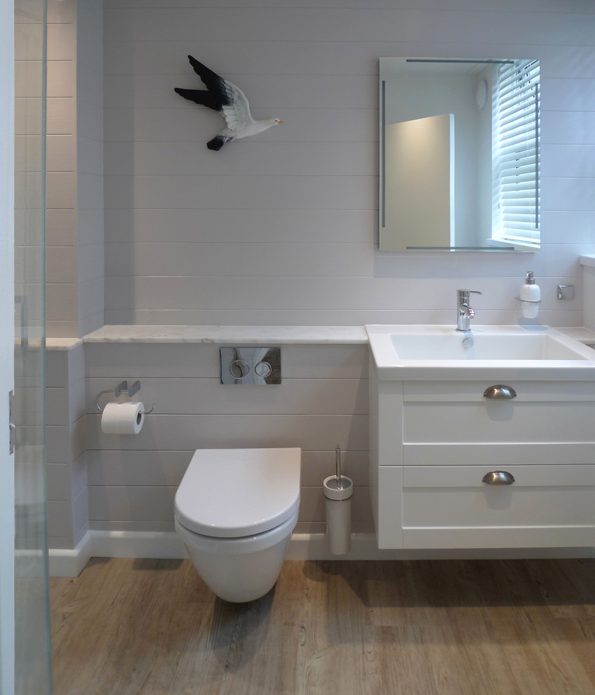 コーンウォールにある小さなビーチスタイルのおしゃれなバスルーム (浴槽なし) (シェーカースタイル扉のキャビネット、白いキャビネット、大理石の洗面台、白いタイル、セラミックタイル、セラミックタイルの床) の写真