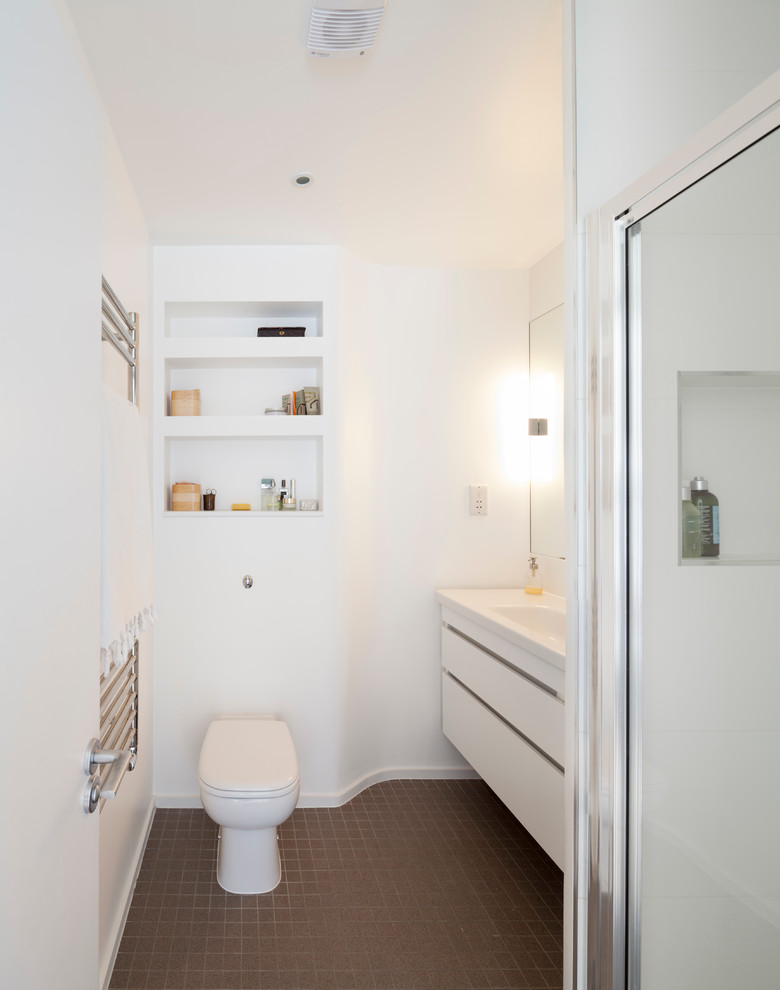 Bild på ett funkis badrum med dusch, med släta luckor, vita skåp, en dusch i en alkov, en toalettstol med hel cisternkåpa och vita väggar