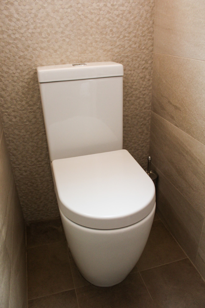 Bild på ett litet funkis toalett, med skåp i ljust trä, en toalettstol med hel cisternkåpa, beige kakel, porslinskakel, beige väggar, klinkergolv i porslin, ett fristående handfat och bänkskiva i kvartsit