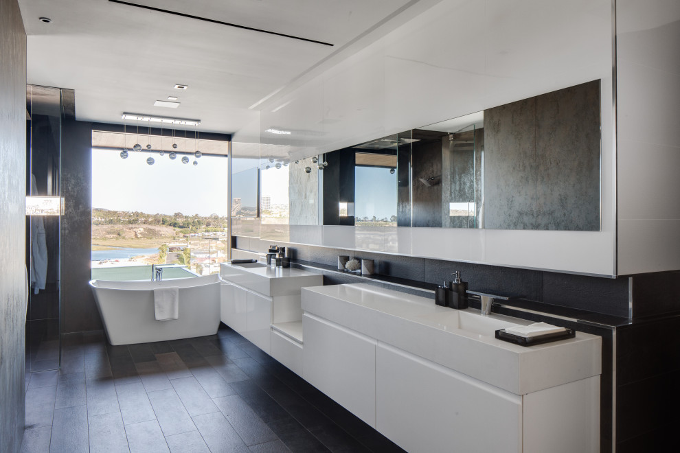 Exemple d'une salle de bain principale tendance avec un placard à porte plane, des portes de placard blanches, une baignoire indépendante, un carrelage noir, un mur blanc, un lavabo intégré, un sol noir et un plan de toilette blanc.