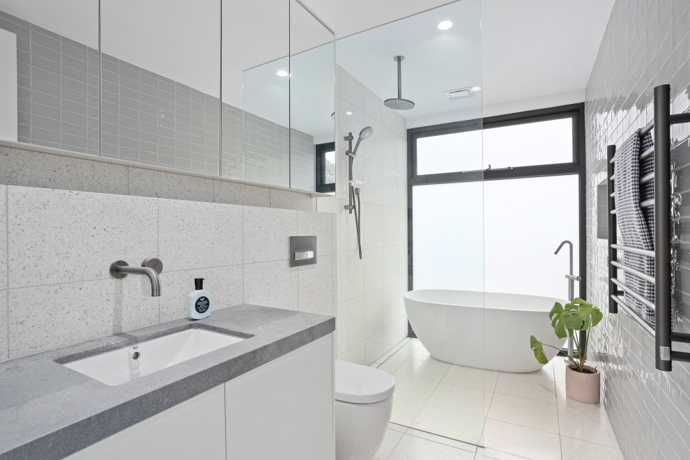 Cette photo montre une salle de bain tendance avec un placard à porte plane, des portes de placard blanches, une baignoire indépendante, un espace douche bain, un lavabo encastré, un plan de toilette blanc et un sol blanc.