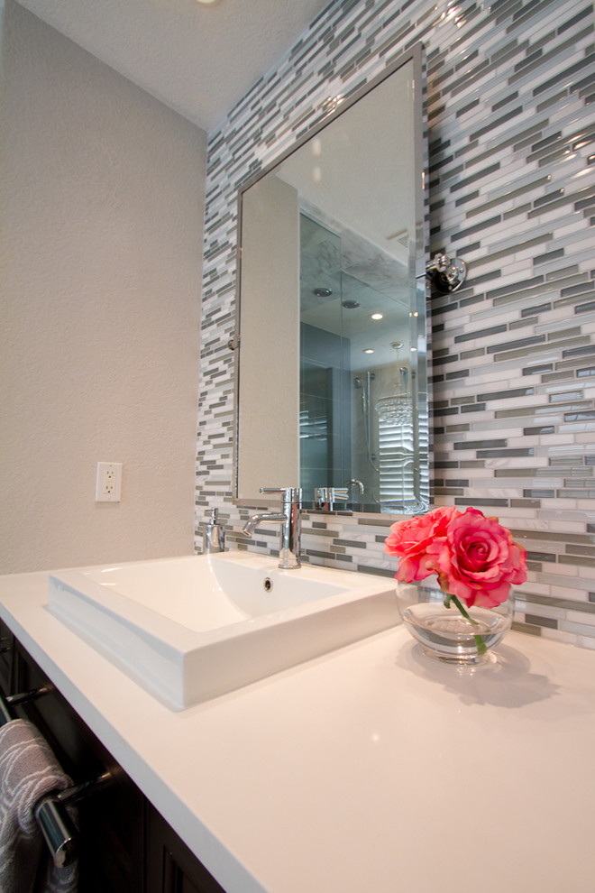 Large modern ensuite bathroom in Denver with recessed-panel cabinets, a freestanding bath, an alcove shower, a two-piece toilet, grey tiles, glass tiles, grey walls, marble flooring, a vessel sink, engineered stone worktops, white floors, a hinged door and dark wood cabinets.