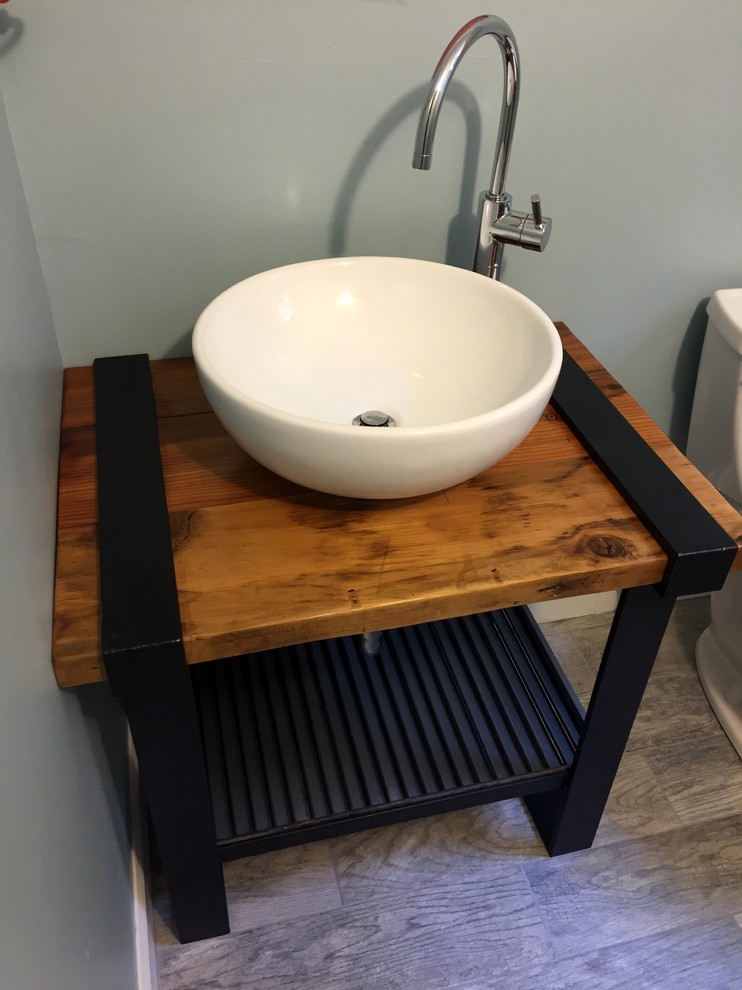 Inredning av ett industriellt litet badrum, med skåp i mellenmörkt trä, en toalettstol med separat cisternkåpa, grå kakel, keramikplattor, blå väggar, klinkergolv i keramik, ett fristående handfat och träbänkskiva