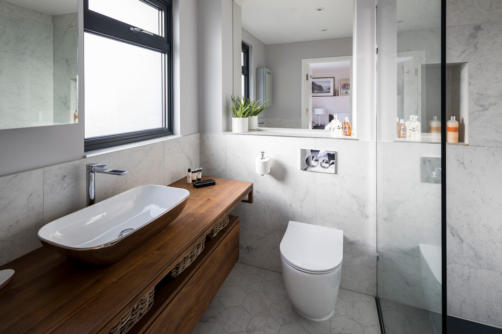 Inspiration for a modern ensuite bathroom in London with freestanding cabinets, brown cabinets, a corner shower, a one-piece toilet, grey tiles, marble tiles, grey walls, lino flooring, a trough sink, wooden worktops, white floors and an open shower.