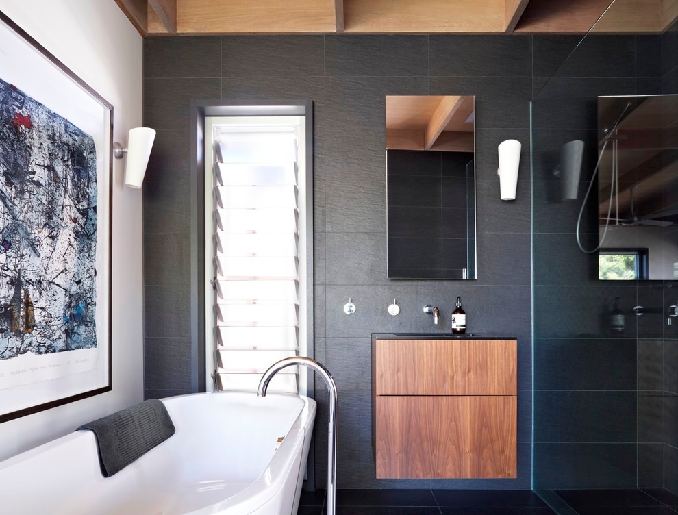 Bild på ett funkis en-suite badrum, med släta luckor, skåp i mellenmörkt trä, ett fristående badkar, en kantlös dusch, svart kakel och vita väggar