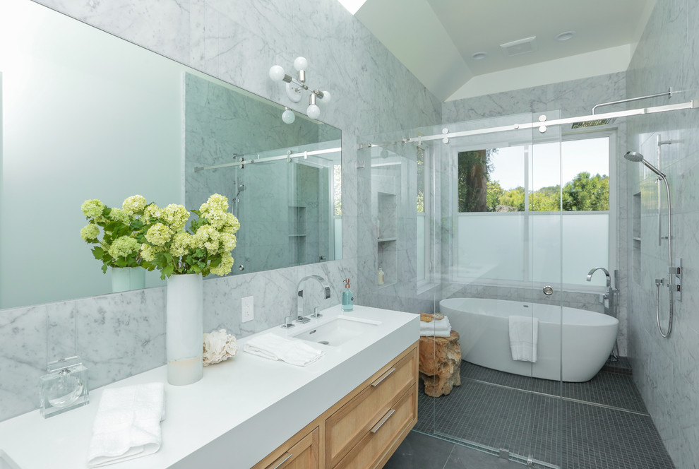 Cette photo montre une salle de bain principale tendance en bois clair avec un placard à porte shaker, une baignoire indépendante, une douche à l'italienne, un carrelage gris, un mur gris, un lavabo encastré, un sol gris et une cabine de douche à porte coulissante.