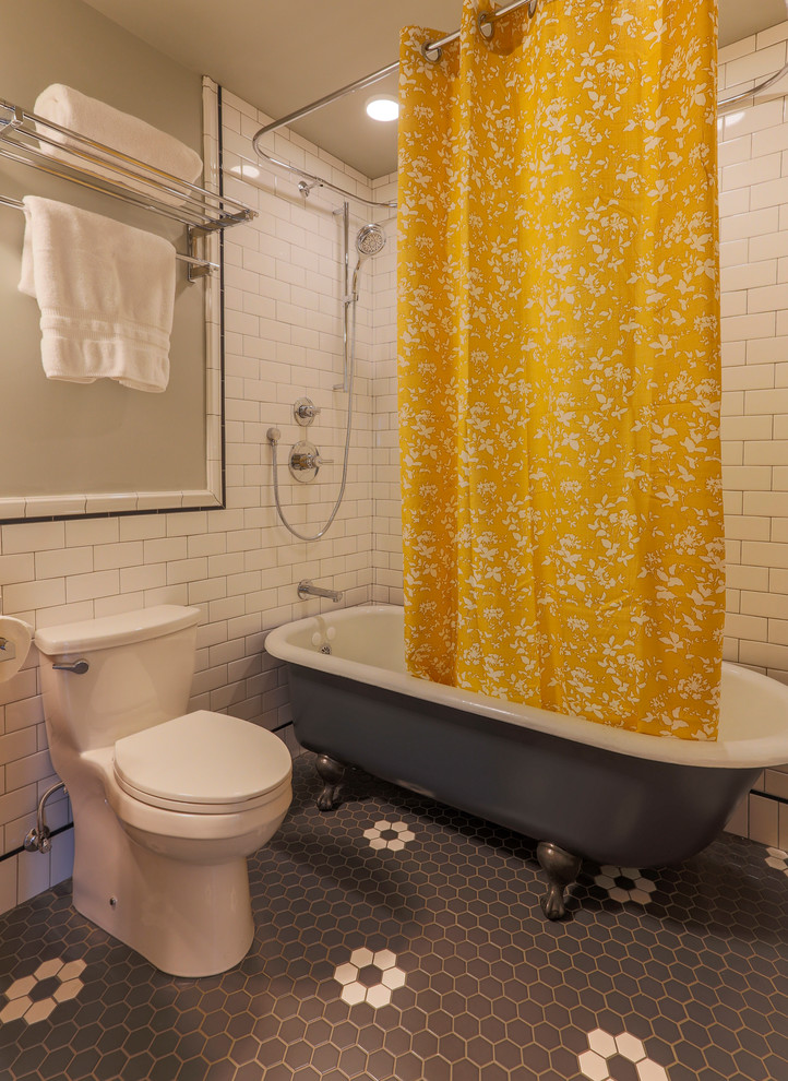Inredning av ett amerikanskt litet badrum, med möbel-liknande, skåp i mellenmörkt trä, ett badkar med tassar, en dusch/badkar-kombination, en toalettstol med hel cisternkåpa, vit kakel, porslinskakel, grå väggar, klinkergolv i porslin, ett undermonterad handfat, bänkskiva i kvarts, flerfärgat golv och dusch med duschdraperi