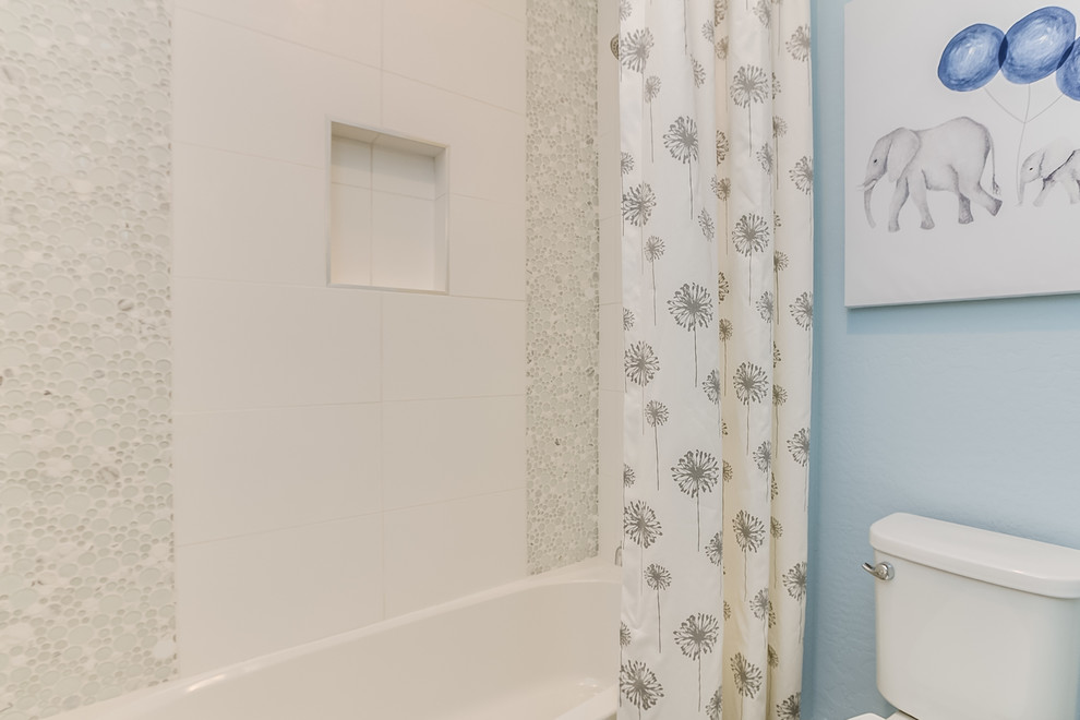 Cette photo montre une grande salle de bain tendance pour enfant avec un placard à porte plane, des portes de placard noires, une baignoire en alcôve, un combiné douche/baignoire, un carrelage gris, des plaques de verre, un mur bleu, un sol en carrelage de céramique, un lavabo encastré, un plan de toilette en surface solide, un sol gris et une cabine de douche avec un rideau.