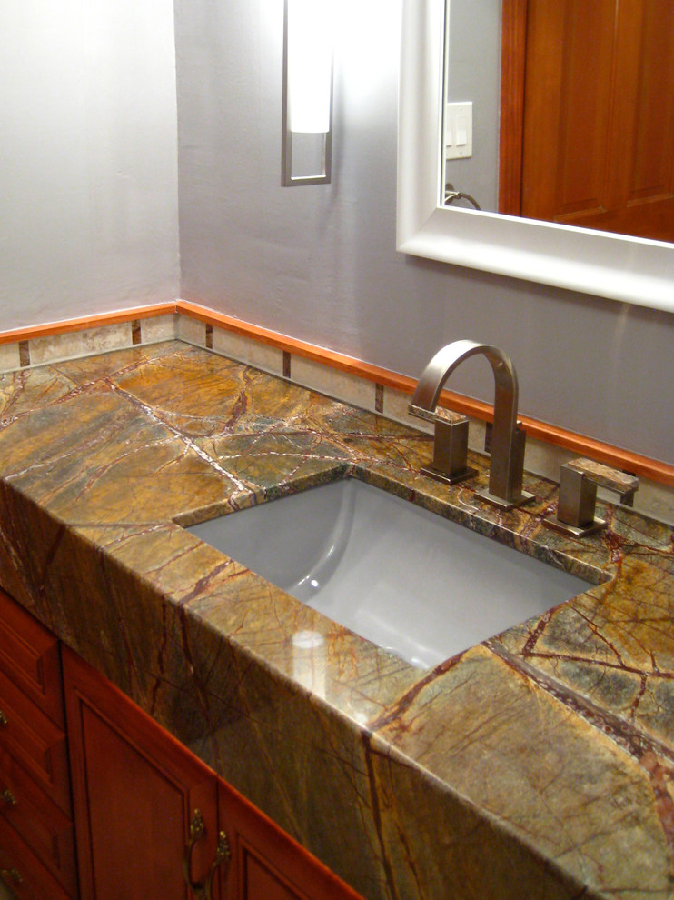 Cette image montre une salle de bain design en bois brun avec un lavabo encastré, un placard avec porte à panneau surélevé, un plan de toilette en marbre et un mur gris.