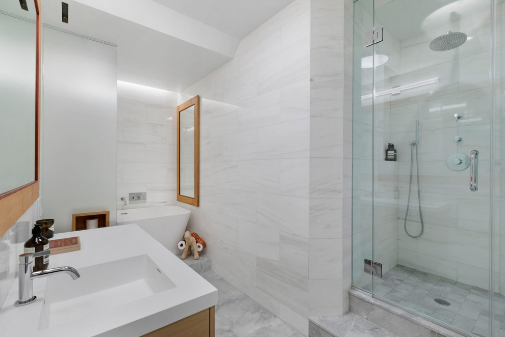 Идея дизайна: ванная комната в современном стиле с светлыми деревянными фасадами, душем в нише, белой плиткой, белыми стенами, монолитной раковиной, серым полом, белой столешницей, нишей и тумбой под одну раковину
