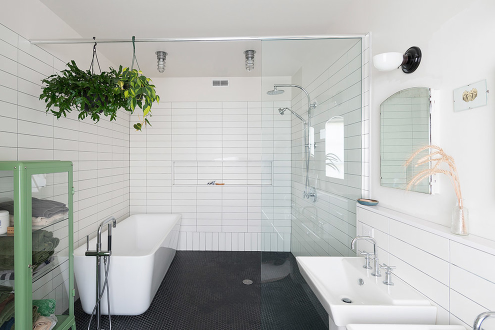 Bild på ett industriellt badrum, med ett väggmonterat handfat, ett fristående badkar, en öppen dusch, vita väggar, mosaikgolv, svart och vit kakel, svart golv och med dusch som är öppen