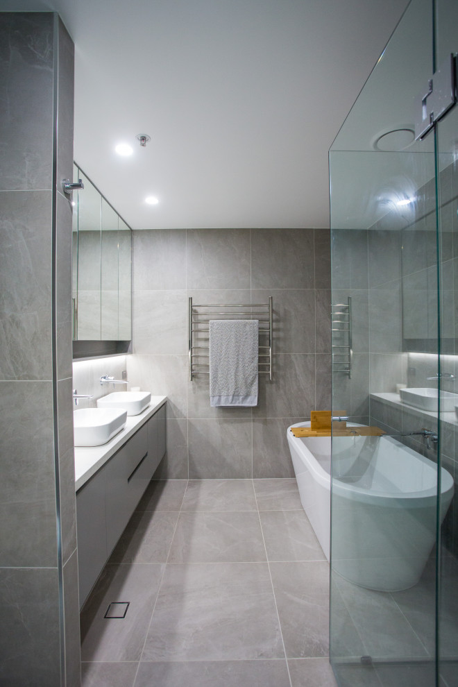 Exemple d'une salle de bain principale moderne de taille moyenne avec un placard à porte plane, des portes de placard grises, une baignoire indépendante, une douche d'angle, WC séparés, un carrelage gris, des carreaux de porcelaine, un mur gris, un sol en carrelage de porcelaine, une vasque, un plan de toilette en quartz modifié, un sol gris, une cabine de douche à porte battante et un plan de toilette blanc.