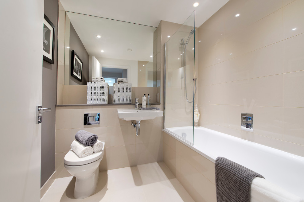 Inredning av ett modernt badrum, med ett badkar i en alkov, en dusch/badkar-kombination, en toalettstol med hel cisternkåpa, beige kakel och grå väggar