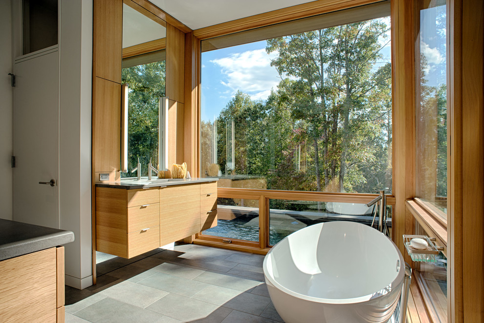 Idées déco pour une salle de bain principale moderne en bois brun avec un placard à porte plane, une baignoire indépendante, un carrelage gris, un sol gris, un mur beige, un sol en carrelage de céramique, un lavabo intégré et un plan de toilette en béton.