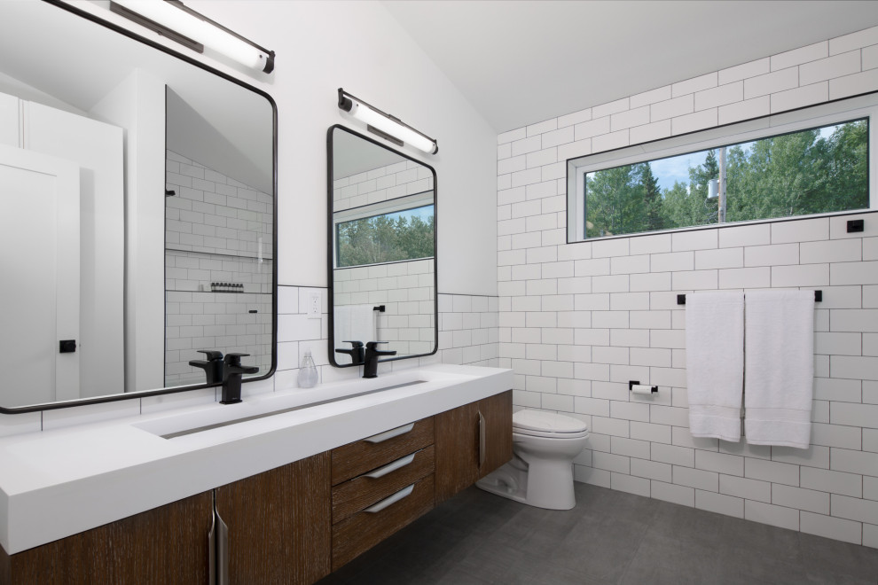 This is an example of a contemporary bathroom in Edmonton with flat-panel cabinets, dark wood cabinets, white tiles, white walls, a trough sink, grey floors, white worktops, double sinks, a floating vanity unit and a vaulted ceiling.
