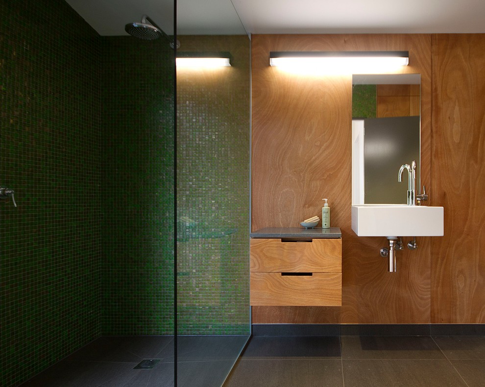 Cette photo montre une salle de bain bord de mer en bois brun de taille moyenne avec un placard en trompe-l'oeil, un carrelage vert, un carrelage en pâte de verre, un plan de toilette en granite, un espace douche bain, WC suspendus, un mur vert, un sol en ardoise, un lavabo suspendu, un sol gris, aucune cabine et un plan de toilette gris.