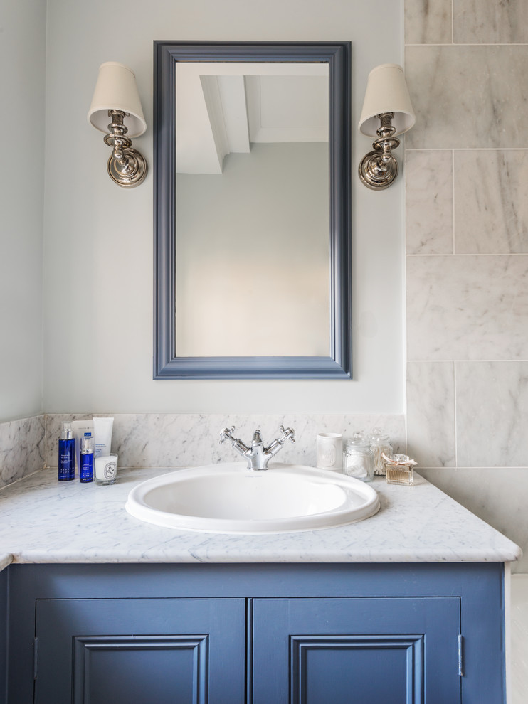 Inspiration for a small traditional bathroom in London with recessed-panel cabinets, blue cabinets, a built-in bath, a shower/bath combination, a two-piece toilet, white tiles, stone tiles, blue walls, marble flooring, a built-in sink and marble worktops.