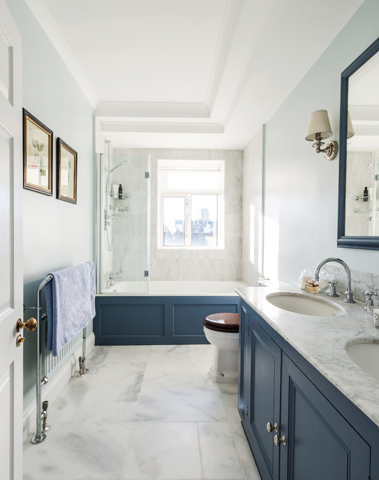 Design ideas for a medium sized classic ensuite bathroom in London with recessed-panel cabinets, blue cabinets, a built-in bath, a shower/bath combination, white tiles, stone tiles, blue walls, marble flooring, a submerged sink and marble worktops.