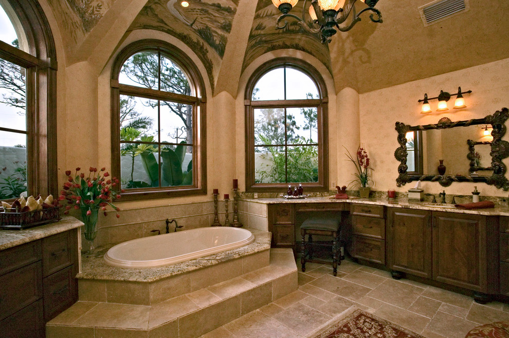 На фото: большая главная ванная комната в средиземноморском стиле с фасадами с выступающей филенкой, темными деревянными фасадами, накладной ванной, унитазом-моноблоком, бежевой плиткой, керамической плиткой, бежевыми стенами, полом из сланца, врезной раковиной, столешницей из гранита и бежевым полом