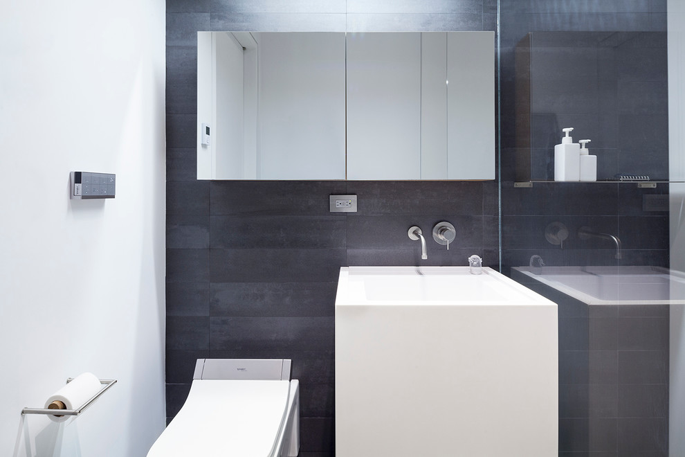 Exempel på ett litet modernt en-suite badrum, med släta luckor, vita skåp, en öppen dusch, en vägghängd toalettstol, grå kakel, porslinskakel, vita väggar, klinkergolv i porslin, ett piedestal handfat och bänkskiva i akrylsten