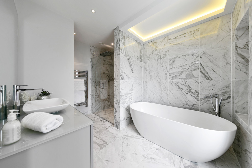 Cette photo montre une salle de bain moderne de taille moyenne avec un placard à porte plane, une baignoire indépendante, une douche d'angle, du carrelage en marbre, un mur gris, un sol en marbre, une vasque, un sol blanc, une cabine de douche à porte battante et un plan de toilette gris.