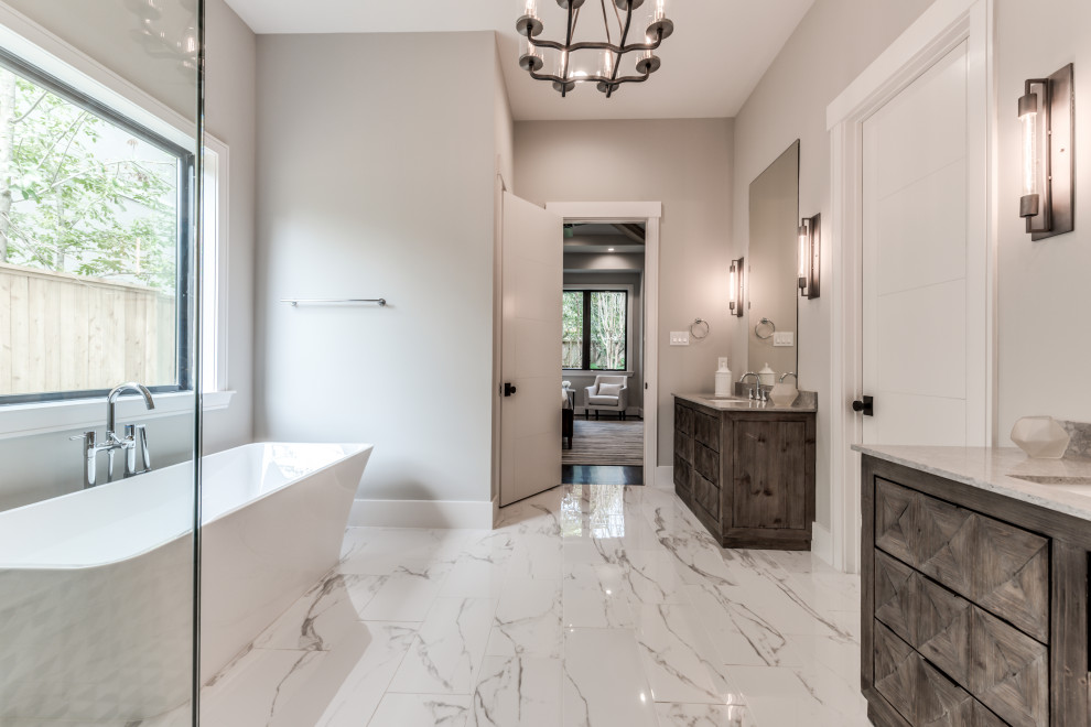 Large modern ensuite bathroom in Houston with freestanding cabinets, brown cabinets, a freestanding bath, a corner shower, a one-piece toilet, white tiles, porcelain tiles, grey walls, porcelain flooring, a submerged sink, marble worktops, white floors, a hinged door and grey worktops.