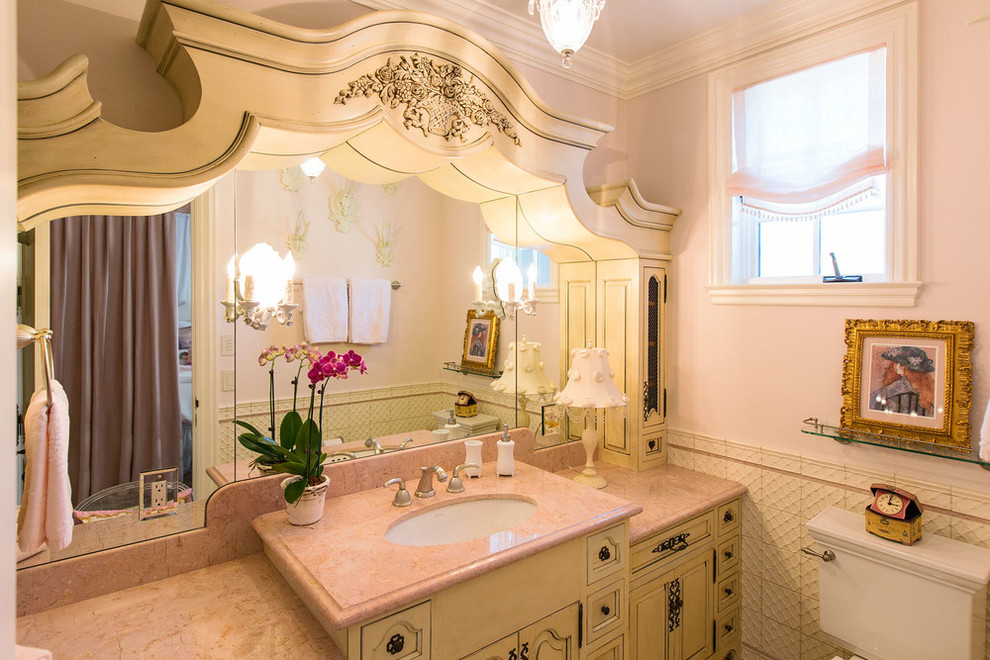 Bild på ett stort vintage badrum för barn, med ett undermonterad handfat, möbel-liknande, vita skåp, marmorbänkskiva, ett platsbyggt badkar, en toalettstol med separat cisternkåpa, vit kakel, porslinskakel, rosa väggar och travertin golv