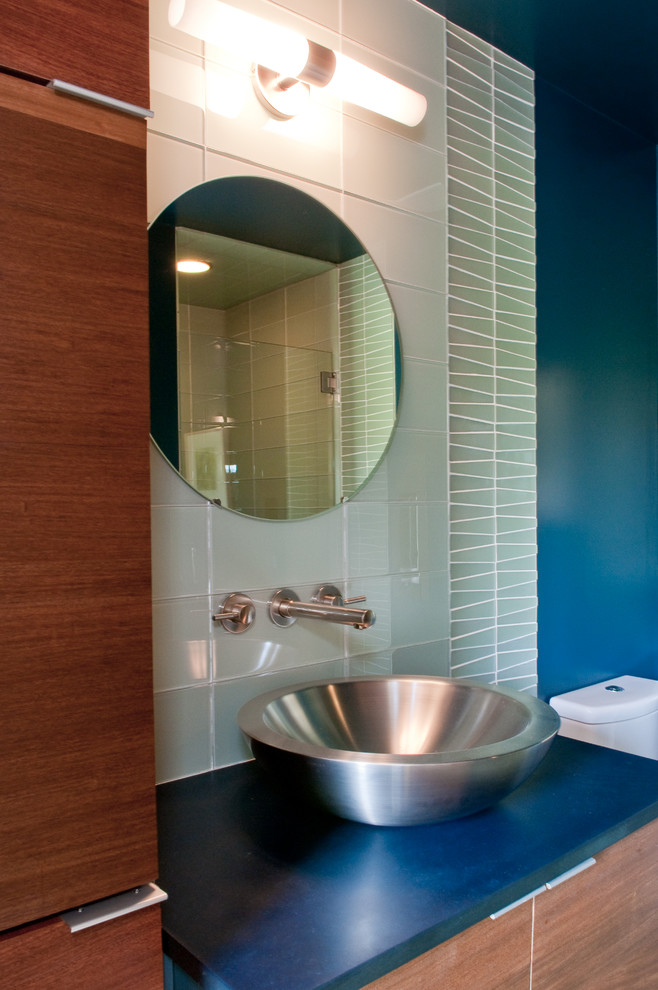 Cette image montre une salle d'eau urbaine en bois brun de taille moyenne avec un placard à porte plane, WC séparés, un carrelage blanc, un carrelage en pâte de verre, un mur bleu, une vasque et un plan de toilette en surface solide.
