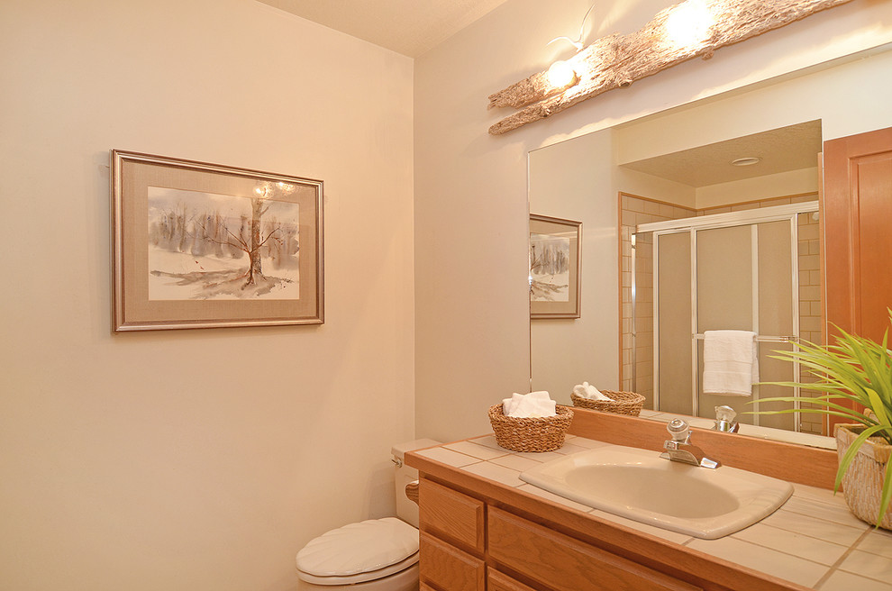 This is an example of a small contemporary bathroom in Seattle with a built-in sink, recessed-panel cabinets, medium wood cabinets, tiled worktops, an alcove shower, white tiles, ceramic tiles, beige walls and vinyl flooring.