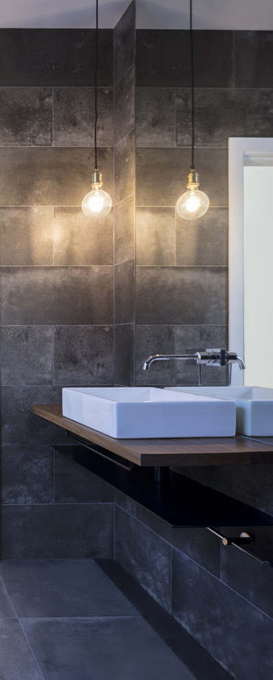 Aménagement d'une salle de bain moderne avec une douche ouverte, un carrelage gris, un plan de toilette en bois, aucune cabine et un mur gris.