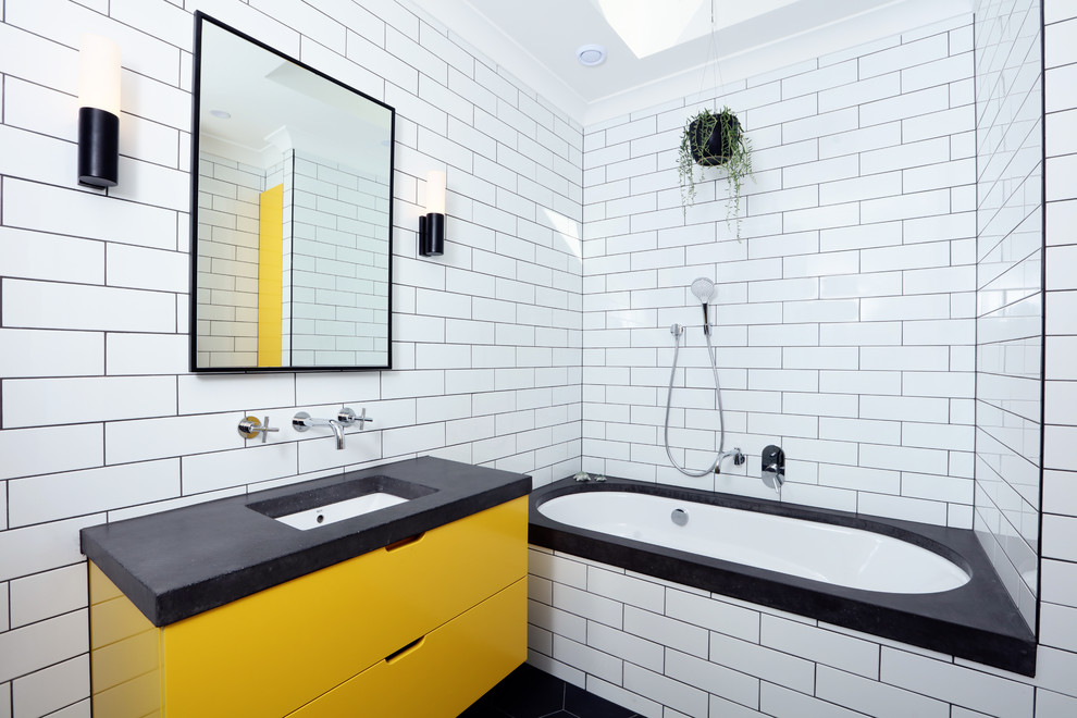 Идея дизайна: детская ванная комната среднего размера в современном стиле с полновстраиваемой ванной, плиткой кабанчик, полом из керамогранита, столешницей из бетона, плоскими фасадами, желтыми фасадами, врезной раковиной, черным полом, серой столешницей, белой плиткой, белыми стенами, тумбой под одну раковину, подвесной тумбой и кирпичными стенами