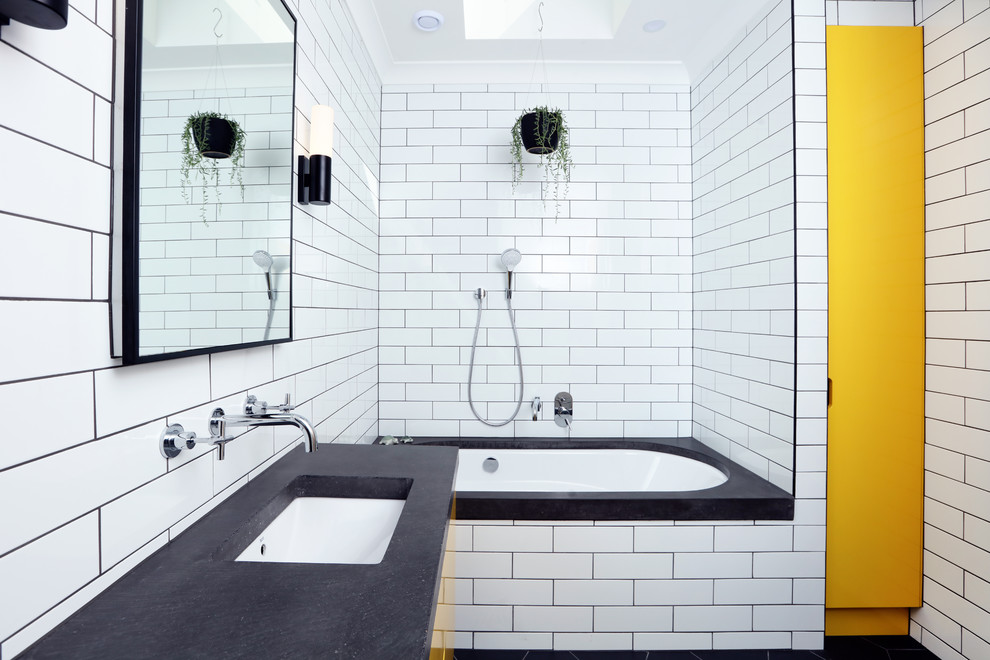 Exemple d'une salle de bain tendance de taille moyenne pour enfant avec un carrelage métro, un sol en carrelage de porcelaine, un plan de toilette en béton, des portes de placard jaunes, une baignoire encastrée, un combiné douche/baignoire, un carrelage blanc, un mur blanc, un lavabo encastré, un sol noir, un plan de toilette gris, meuble simple vasque, meuble-lavabo suspendu et un mur en parement de brique.