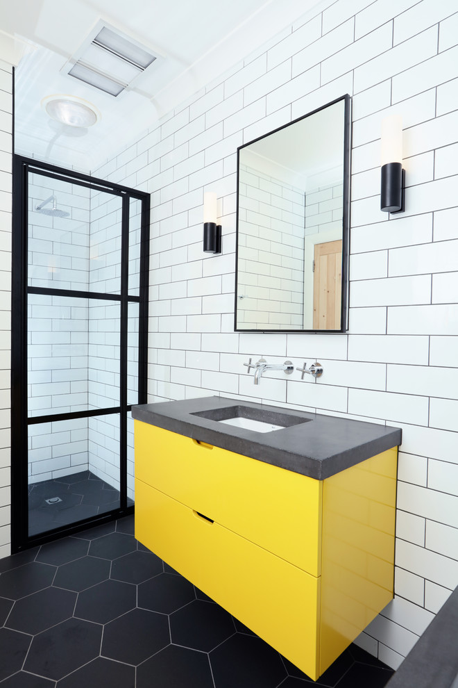 На фото: детская ванная комната среднего размера в современном стиле с плиткой кабанчик, полом из керамогранита, столешницей из бетона, плоскими фасадами, желтыми фасадами, полновстраиваемой ванной, душем в нише, белой плиткой, белыми стенами, врезной раковиной, черным полом, душем с раздвижными дверями, серой столешницей, тумбой под одну раковину, подвесной тумбой и кирпичными стенами