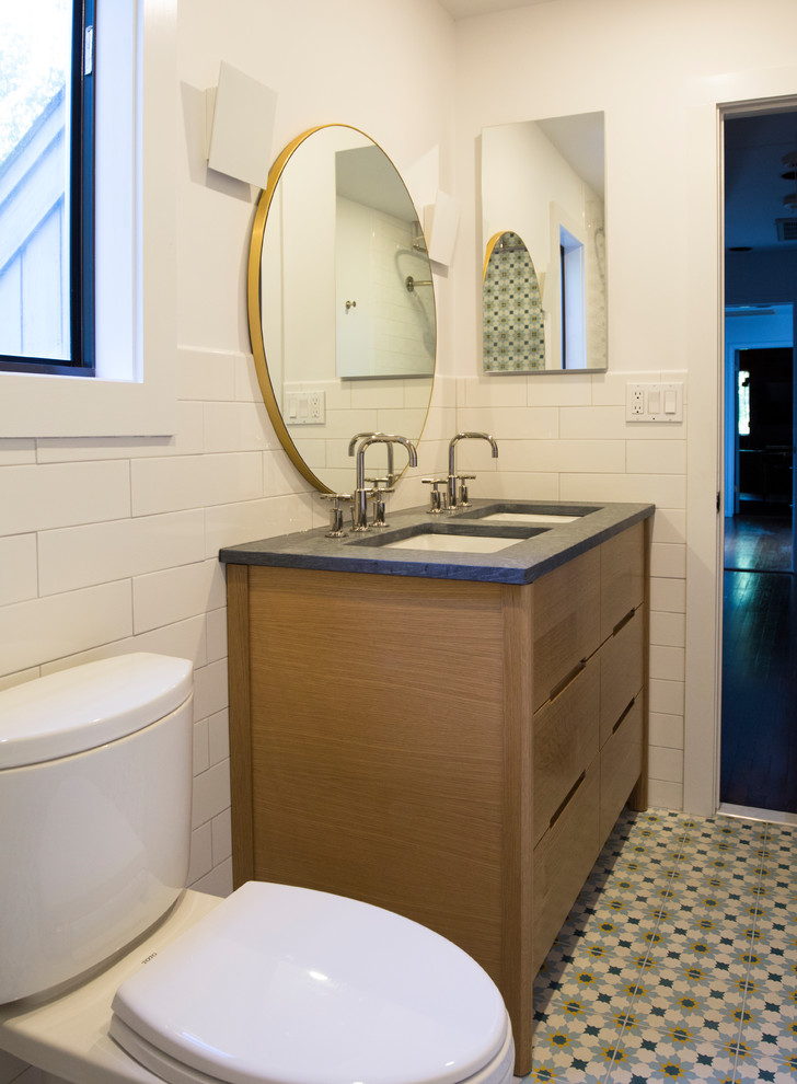 Photo of a medium sized classic family bathroom in New York with freestanding cabinets, light wood cabinets, a freestanding bath, a shower/bath combination, a one-piece toilet, multi-coloured tiles, cement tiles, multi-coloured walls, cement flooring, a built-in sink, soapstone worktops, multi-coloured floors, a shower curtain and grey worktops.