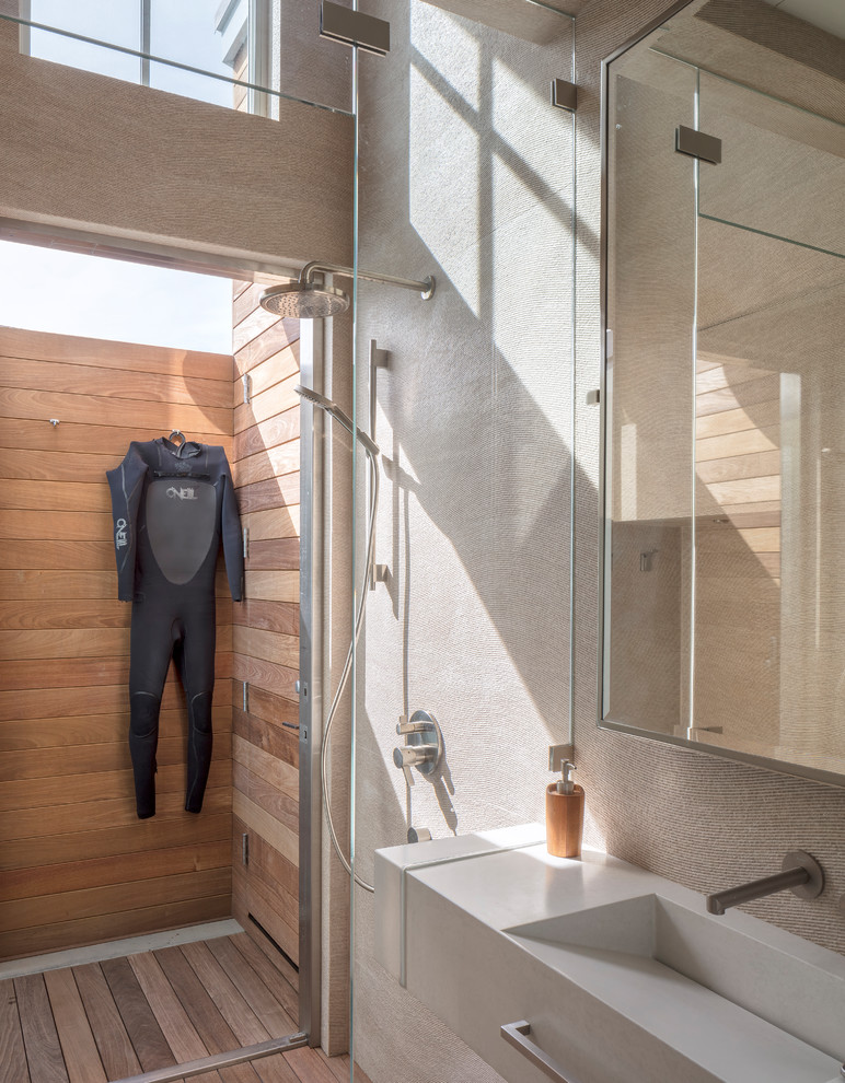Exempel på ett litet maritimt beige beige badrum, med öppna hyllor, beige skåp, en kantlös dusch, en vägghängd toalettstol, beige kakel, porslinskakel, beige väggar, mellanmörkt trägolv, ett avlångt handfat, bänkskiva i betong och dusch med gångjärnsdörr