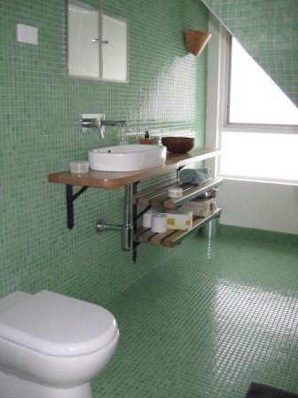 Пример оригинального дизайна: маленькая главная ванная комната в современном стиле с открытыми фасадами, коричневыми фасадами, накладной ванной, душем над ванной, унитазом-моноблоком, зеленой плиткой, плиткой мозаикой, зелеными стенами, полом из мозаичной плитки, настольной раковиной, столешницей из дерева, зеленым полом, душем с распашными дверями и коричневой столешницей для на участке и в саду