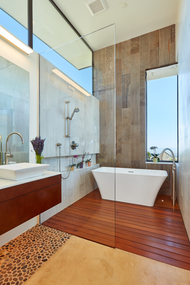 На фото: ванная комната в современном стиле с плоскими фасадами, темными деревянными фасадами, отдельно стоящей ванной, открытым душем, коричневой плиткой, белыми стенами, полом из галечной плитки, настольной раковиной и открытым душем с
