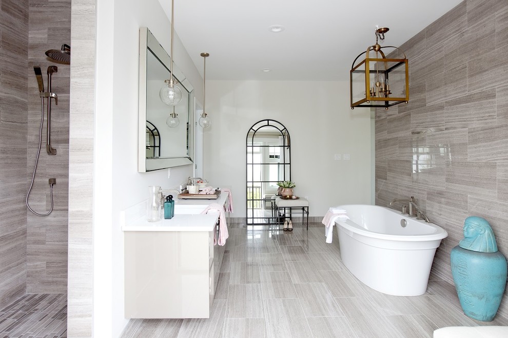 Cette image montre une salle de bain traditionnelle avec un lavabo encastré, un placard à porte plane, des portes de placard grises, une baignoire indépendante, un carrelage gris, un mur blanc et un sol gris.