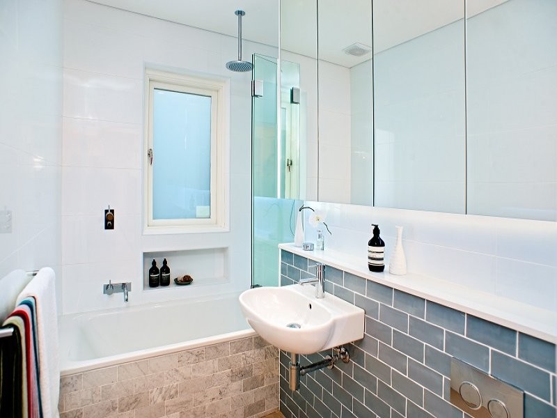 Modern inredning av ett litet badrum, med ett väggmonterat handfat, släta luckor, kaklad bänkskiva, en dusch/badkar-kombination och tunnelbanekakel