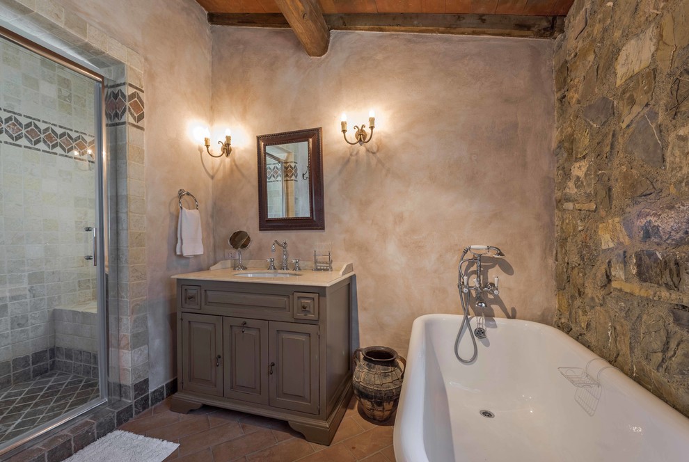 Lantlig inredning av ett mellanstort en-suite badrum, med möbel-liknande, grå skåp, ett badkar med tassar, stenkakel och klinkergolv i terrakotta