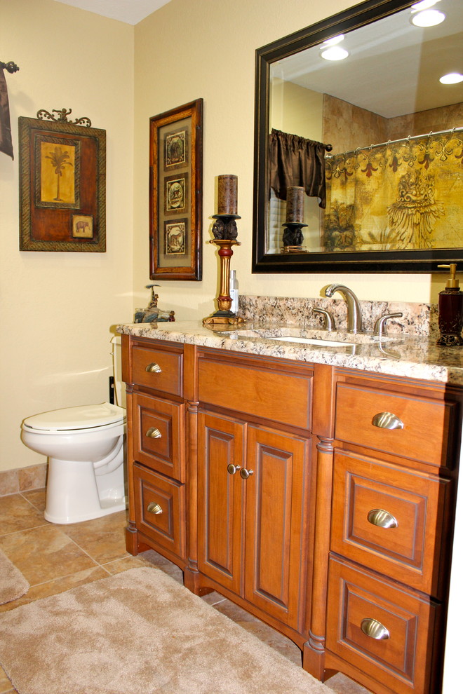 Cette image montre une salle d'eau traditionnelle en bois clair avec un lavabo encastré, un placard avec porte à panneau encastré, un plan de toilette en granite, une douche d'angle, WC à poser, un carrelage beige, des carreaux de porcelaine, un mur beige et un sol en carrelage de porcelaine.