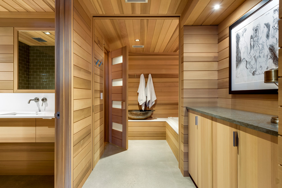 Modelo de sauna rústica con armarios con paneles lisos, puertas de armario de madera clara, lavabo bajoencimera, suelo gris, encimeras blancas y suelo de cemento