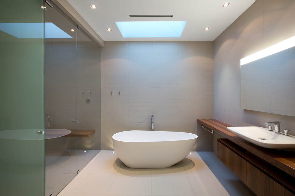 Design ideas for a large modern bathroom in Vancouver with a vessel sink, freestanding cabinets, medium wood cabinets, wooden worktops, a freestanding bath, a built-in shower, a wall mounted toilet, grey tiles, porcelain tiles and porcelain flooring.
