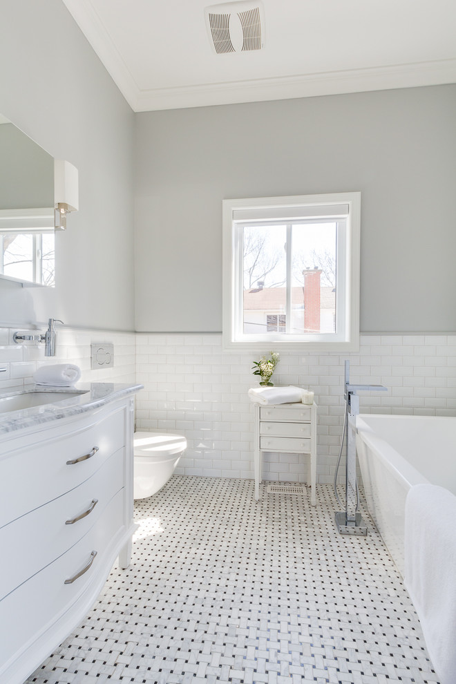 Photo of a medium sized traditional shower room bathroom in Montreal with beaded cabinets, white cabinets, a freestanding bath, a wall mounted toilet, white tiles, marble tiles, grey walls, marble flooring, a submerged sink and marble worktops.