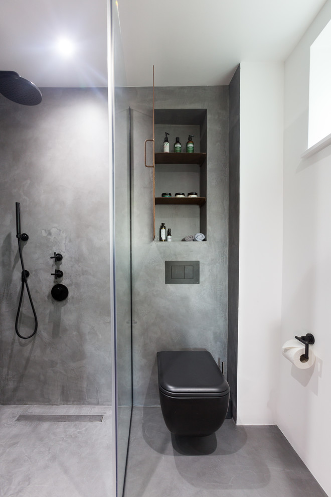 Inredning av ett industriellt litet en-suite badrum, med luckor med profilerade fronter, bruna skåp, en öppen dusch, en vägghängd toalettstol, grå kakel, grå väggar, betonggolv, ett väggmonterat handfat, grått golv och dusch med gångjärnsdörr