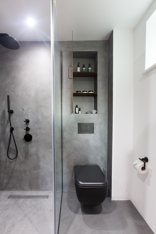 Kleines Industrial Badezimmer En Suite mit Kassettenfronten, braunen Schränken, offener Dusche, Wandtoilette, grauen Fliesen, grauer Wandfarbe, Betonboden, Wandwaschbecken, grauem Boden und Falttür-Duschabtrennung in London