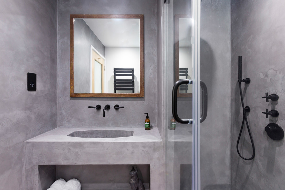 Photo of a small industrial ensuite bathroom in London with beaded cabinets, brown cabinets, a walk-in shower, a wall mounted toilet, grey tiles, grey walls, concrete flooring, a wall-mounted sink, grey floors and a hinged door.